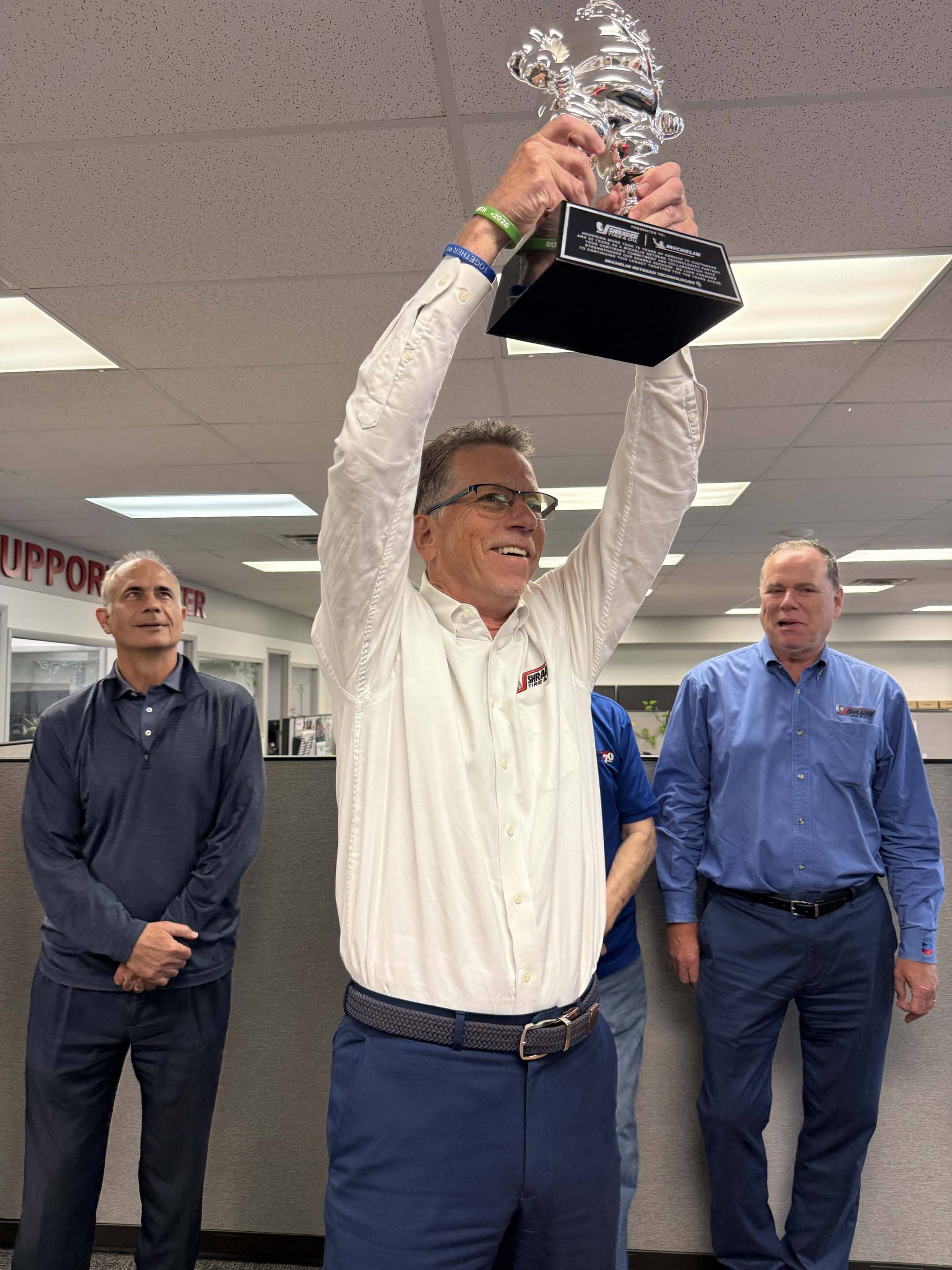 Joe Shrader of Shrader Tire & Oil raising the Michelin Retread Technologies Bibendum trophy overhead at Toledo headquarters